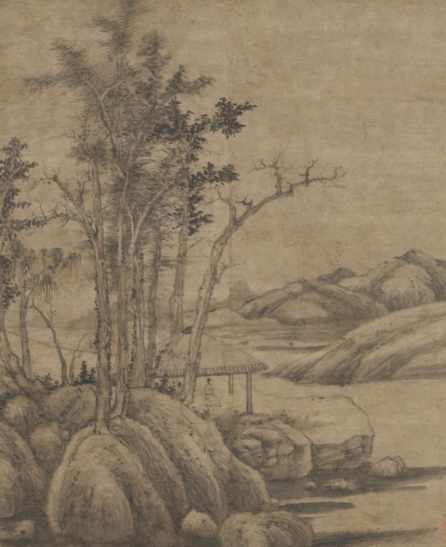 A tall, spare ink landscape on pale paper: a stand of slender autumn trees on a rocky bank, a small thatched open pavilion with a single standing figure, and low bare hills across quiet water beyond.
